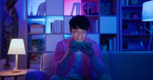 asian man plays mobile games on sofa in the evening at home