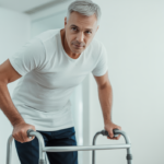 Photorealistic image of a middle-aged patient using a walker during hip replacement recovery in a clean, bright environment